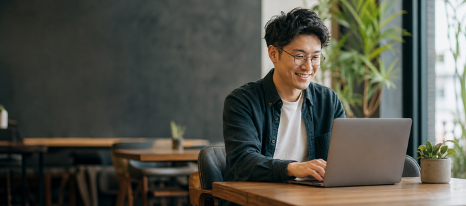 Happy Asian Student With Glasses Using Laptop In Cafe-1